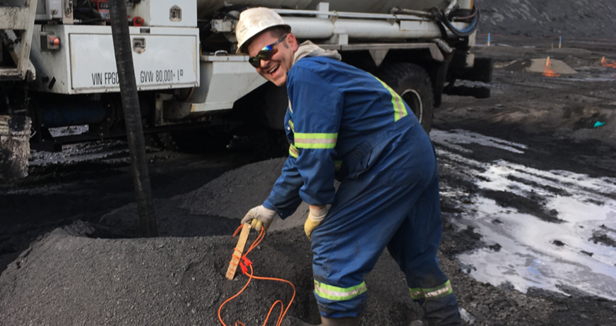 Person in safety gear holding an orange cable next to industrial equipment in a worksite.